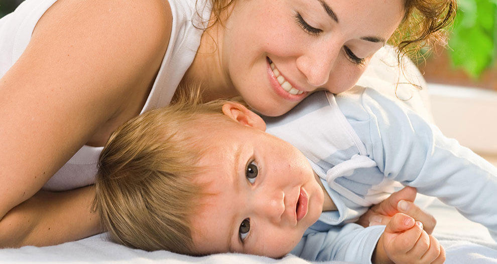 A woman and a baby are lying on a bed.